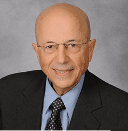 Professional portrait of an elderly man with glasses in a suit and tie.