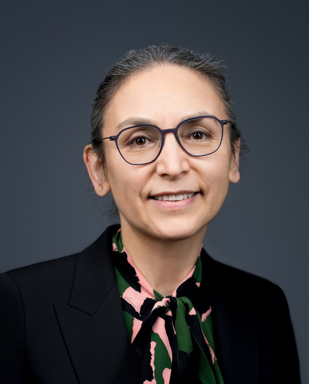 Professional woman wearing glasses and a black blazer smiles confidently.