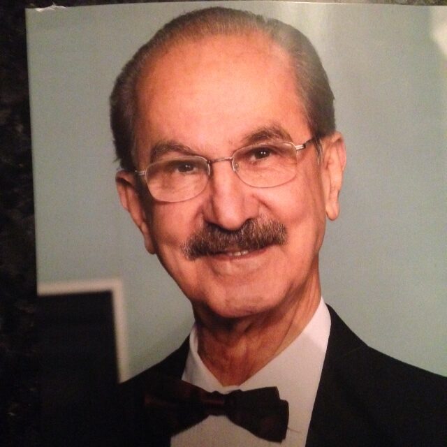 Elderly man with glasses and mustache in formal wear.