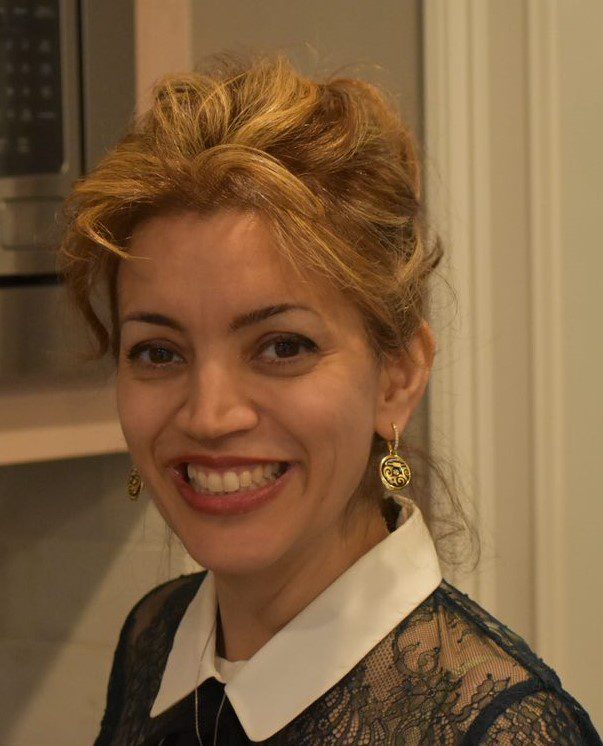 Smiling woman with blonde hair and earrings indoors.