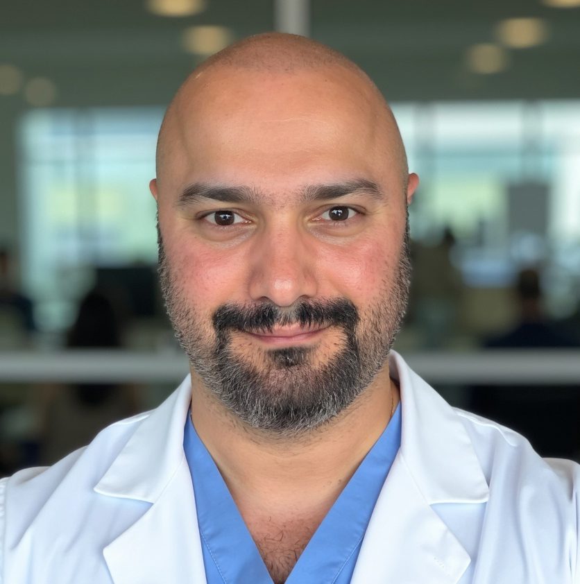 Smiling bald man in a white lab coat in a bright office.