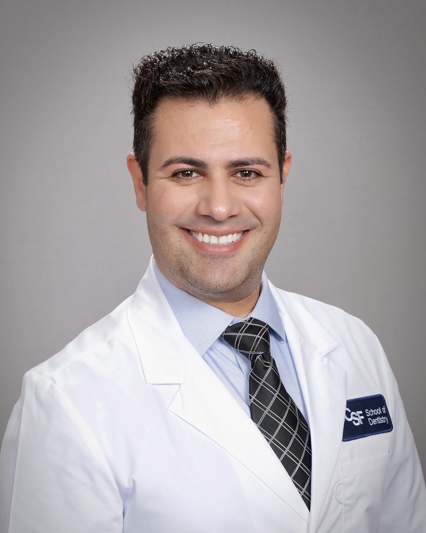Smiling male doctor in white coat with gray background.